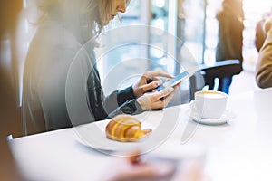 Young woman holding in female hands mobile phone and drink hot aroma coffee or tea in breakfast time, hipster traveler girl