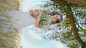 Young woman holding flowers at rye field vertical. Tender lady posing at nature