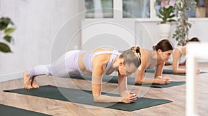 Young woman holding forearms plank pose in yoga studio