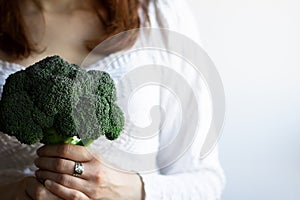 Young woman holding fresh broccoli vegetable in her hands isolated on white background, a closeup