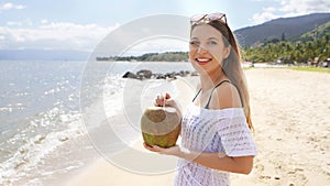 Young woman holding a fresh coconut enjoying on tropical beach. Healthy girl relaxing on the beach in her holiday holding a green
