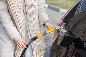 Young woman holding a fuel nozzle in her hand while refueling car at gas station.