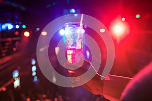 Young woman holding a glass with cocktail in disco lights.