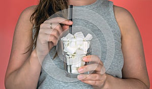 Young woman holding a glass filled with sugar cubes and a straw on pink background, Sweets,diet,fast food,unhealthy eating concept