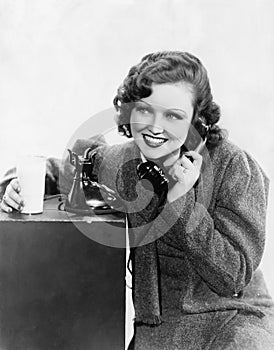 Young woman holding a glass of milk and talking on a rotary phone photo