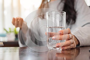 Young woman holding glass of water and taking pill at home