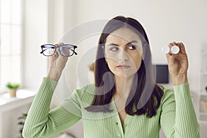 Young woman holding glasses and eye lenses and hesitating which solution to choose