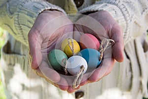 Young woman holding in hands decorative colorful Easter eggs on twine, outdoors, sun flecks