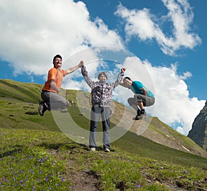 Young woman holding hands with two laughing man on a background of mountains