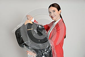 Young woman holding hanger with dress on grey background. Dry-cleaning service