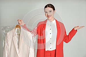 Young woman holding hanger with jacket on grey background. Dry-cleaning service