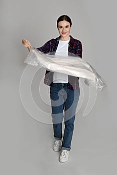 Young woman holding hanger with jacket on grey background. Dry-cleaning service