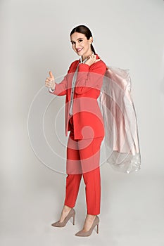 Young woman holding hanger with jacket on grey background. Dry-cleaning service