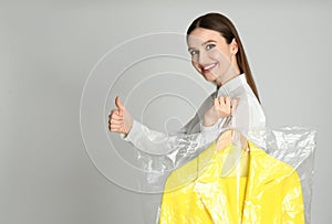 Young woman holding hanger with jacket on grey background. Dry-cleaning service