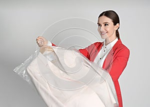 Young woman holding hanger with jacket on grey background. Dry-cleaning service