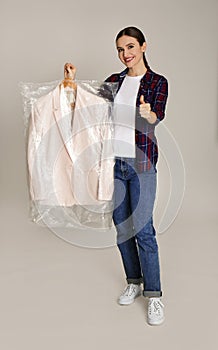 Young woman holding hanger with jacket on grey background. Dry-cleaning service