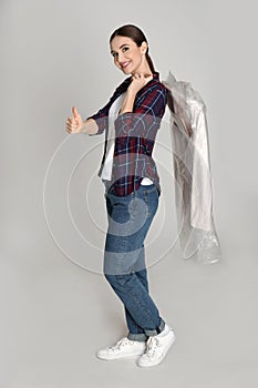 Young woman holding hanger with jacket on grey background. Dry-cleaning service