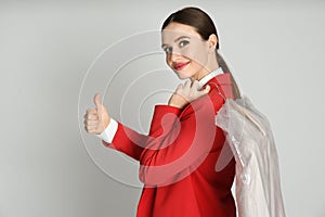 Young woman holding hanger with jacket on light grey background. Dry-cleaning service