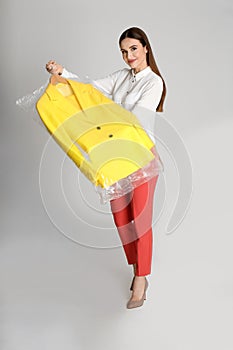 Young woman holding hanger with jacket on light grey background. Dry-cleaning service