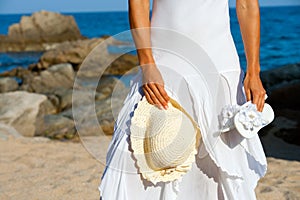 Young woman holding hat and flip flops on beach.