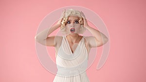 Young woman holding her head in shock, surprise. A woman in the style of Marilyn Monroe in the studio on a pink