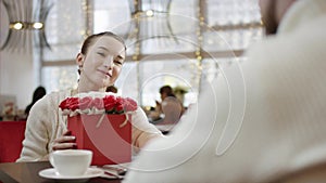 Young woman is holding her husband hand and staring to his eyes with box of flowers in other hand in restaurant