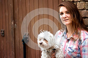 Young woman holding her little dog and standing at brick wall