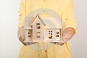 Young woman holding house model on light background