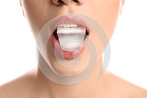 Young woman holding ice cube in mouth on white background