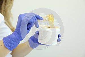 Young woman holding liquid yellow paste for shugaring on white background