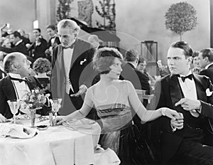 Young woman holding a man's hand at a different table while her companion is talking to the waiter