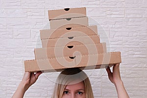 Young woman holding many stacked carton pizza boxes of different sizes on the head, restaurant to home delivery concept