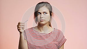 Young woman holding medical pregnancy test on pink studio background, girl is upset and dissapointed with negative result, concept