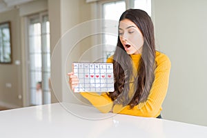 Young woman holding menstruation calendar scared in shock with a surprise face, afraid and excited with fear expression