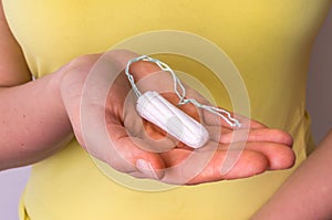 Young woman holding menstruation tampon in hand