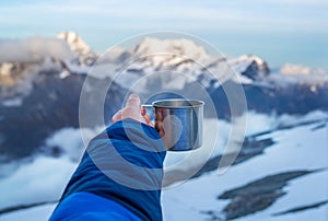 Young woman holding a metal hot tea cup during sunset time from the Mera Peak high camp with snowy seven-thousander mountains. photo