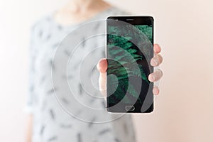 Young woman holding mobile phone with copy space, showing her black blank screen to the camera. People and technology.