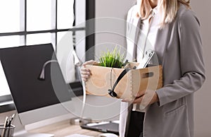 Young woman holding moving box with office stuff indoors