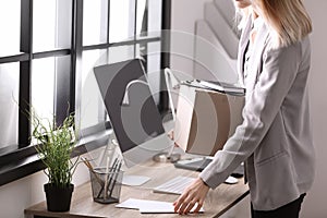 Young woman holding moving box with office stuff indoors