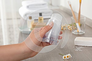 Young woman holding  crystal alum deodorant at wooden table, closeup