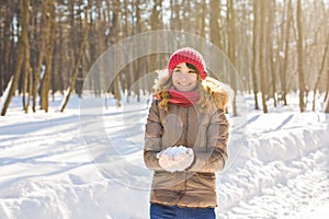 Young woman holding natural soft white snow in her hands to make a snowball, smiling during a cold winter day in the