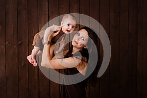 Young woman holding a newborn baby in her arms on the  brown background. Newborn photosession. Family portrait. Mother is kissing