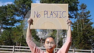 The young woman holding `No Plastic` Poster showing a sign protesting against plastic pollution in the forest. The concept of Worl