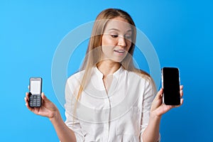 Young woman holding old and new telephone against blue background