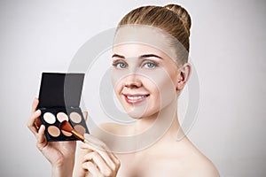 Young woman holding palette for contouring face.