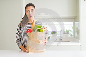 Young woman holding paper bag full of groceries scared in shock with a surprise face, afraid and excited with fear expression