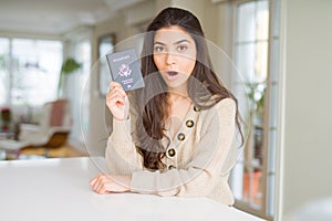 Young woman holding passport of United States of America scared in shock with a surprise face, afraid and excited with fear