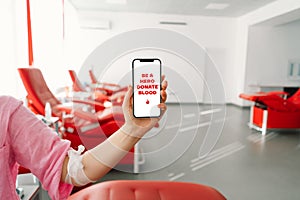 Woman is holding a phone with the inscription Be a Hero Give Blood