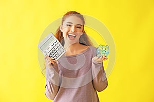 Young woman holding piggy bank and calculator on color background. Money savings concept