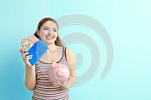 Young woman holding piggy bank and wallet with dollar banknotes on color background. Money savings concept